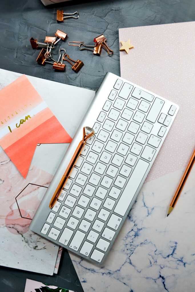 Wellness Portrait-dark-grey-background-with-scattered-pink-papers-copper-bulldog-clips-and-pens-Card-that-says-actually-I-can