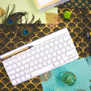 -Black_and-gold-background-with-green-papers-paperweight-silver-keyboard-peacock-feathers-and-gold-filagree-leaves-scaled