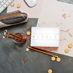 dark-grey-background-with-scattered-pink-papers-paperclips-and-wooden-charms-Sticky-notepad-pencil-case-silver-keyboard-and-mouse-scaled