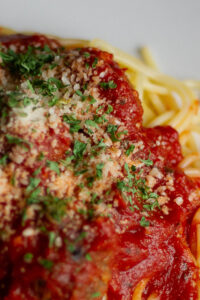 Close up shot of spaghetti sauce on noodles with parmesan cheese and parsley.