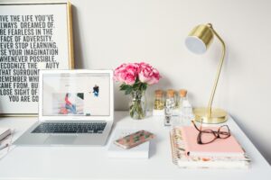Close up of desk with pink flowers, gold lamp, computer, and personal affects.