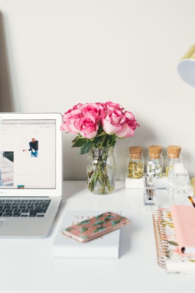 Close up of desk with pink flowers, gold lamp, computer, and personal affects in office.