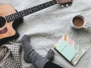 A bed with a guitar, feet with socks on, coffee and a journal that says dreams.