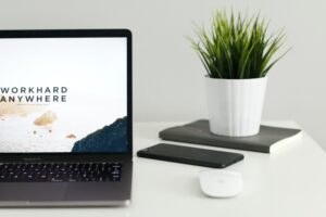 close up of desk with open computer, small plant, and phone on desk.