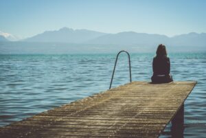 Disappointed person sitting on dock looking out over water with mountains in background