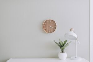 empty white desk with only a small plant, lamp and wall clock.