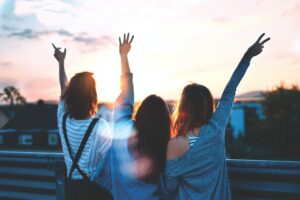A view of friends from behind looking at the sunset with their hands raised