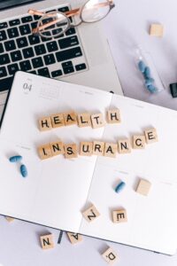 Scrabble tiles spelling out Health insurance on desk with pills and computer