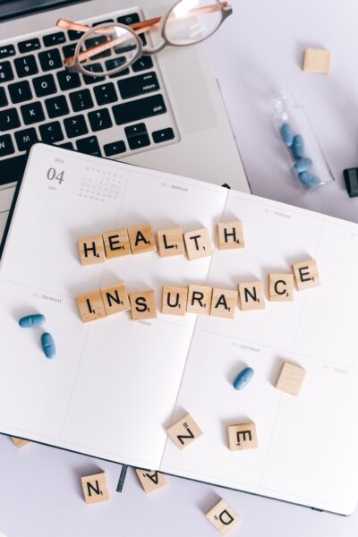 Scrabble tiles spelling out Health insurance on desk with pills and computer