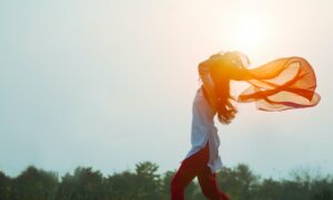 girl with sweater blowing in breeze in front of sunset and trees
