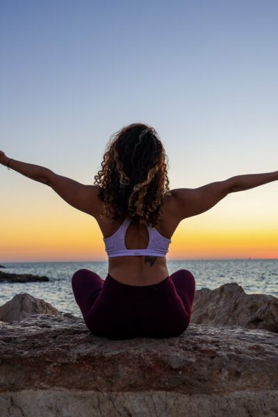 yoga girl on rocks in front of ocean and sunset