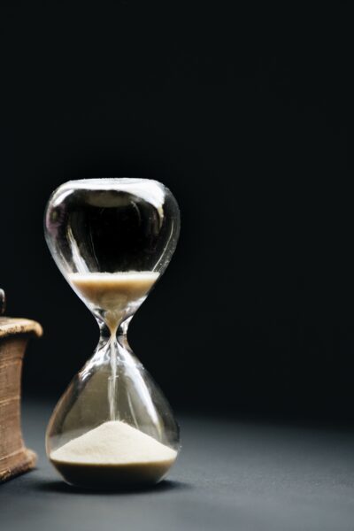 glass hourglass with sand sitting on desk next to purple flowers