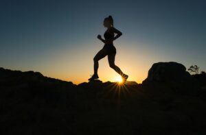 outline of female running with sunset in background