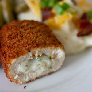 close up picture of stuffed chicken breast, loaded mashed potatoes, and green beans on plate.