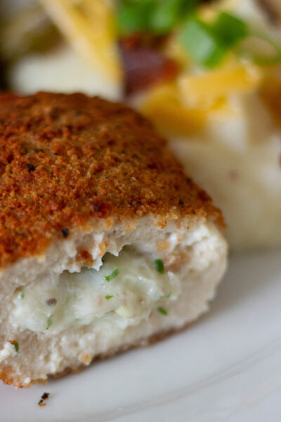 close up picture of stuffed chicken breast, loaded mashed potatoes, and green beans on plate.