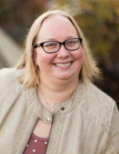 headshot of blond woman wearing black glasses leaning on a rail.