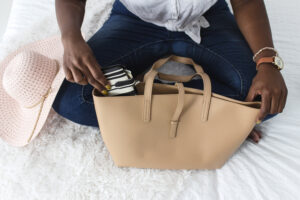 Tan purse on bed with woman in jeans taking out wallet