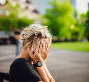 girl with hands over her face sitting on a bench in town