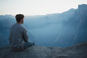 person sitting on a cliff looking out over hills