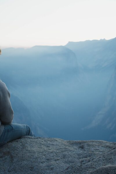 person sitting on a cliff looking out over hills