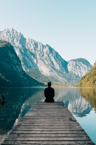 Girl sitting on a wooden dock looking at a calm lake and mountains on a clear day