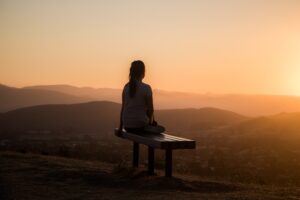 silhouette of woman sitting on bench looking at gold sunset and hills