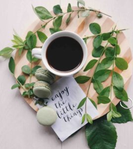 Coffee coup with green leaves around it and a note saying "enjoy the little things"