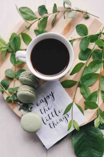 Coffee coup with green leaves around it and a note saying "enjoy the little things"
