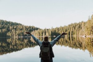 person from behind looking over a lake with arms outstretched