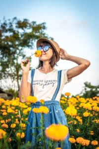 girl in white t-shirt standing in a field of yellow flowers smelling one