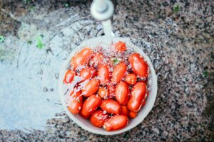 Wash a colander of tomatoes in a sink