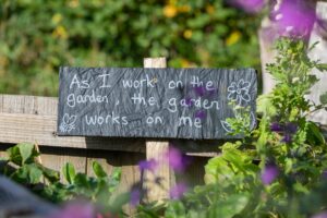 Sign in a garden saying As I work in the garden, the garden works on me.