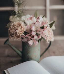 Pink flowers in metal watering can, on a desk with a blank journal