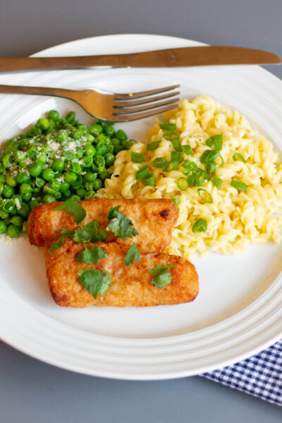 white plate with fish sticks, cheesy pasta, and peas