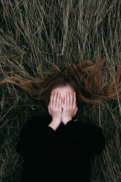 girl laying on her back covering face with hands, hair splayed out