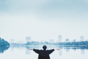 person standing in front of distant city holding arms outstretched